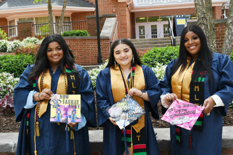 three students wearing MLT stoles and showing off their graduation caps