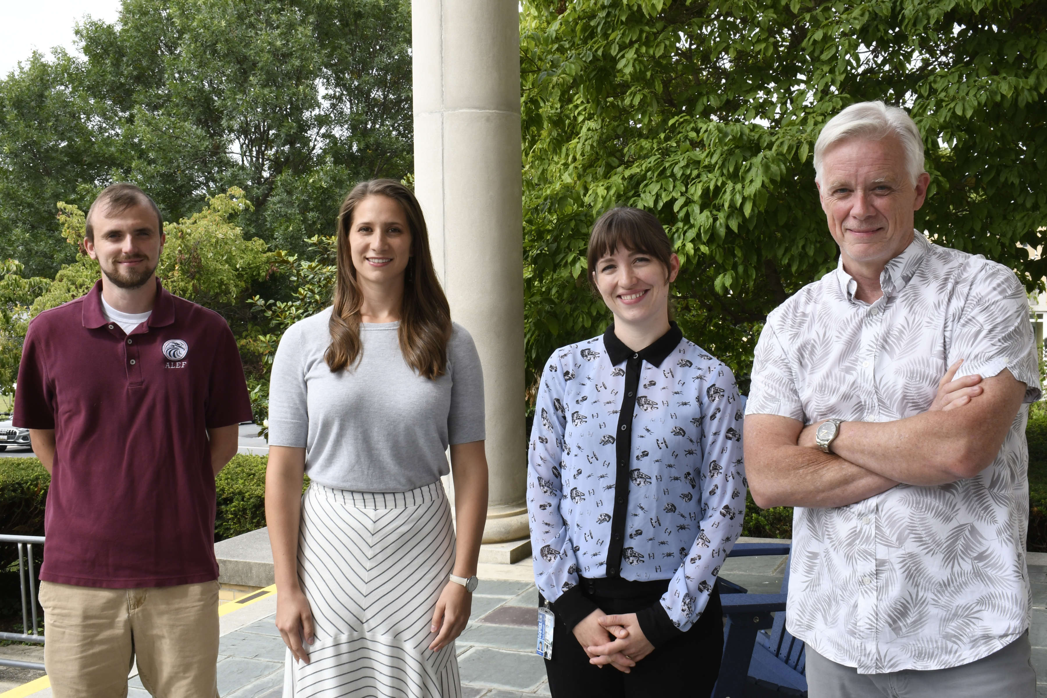 Group of four news professors standing on library porch looking at camera.