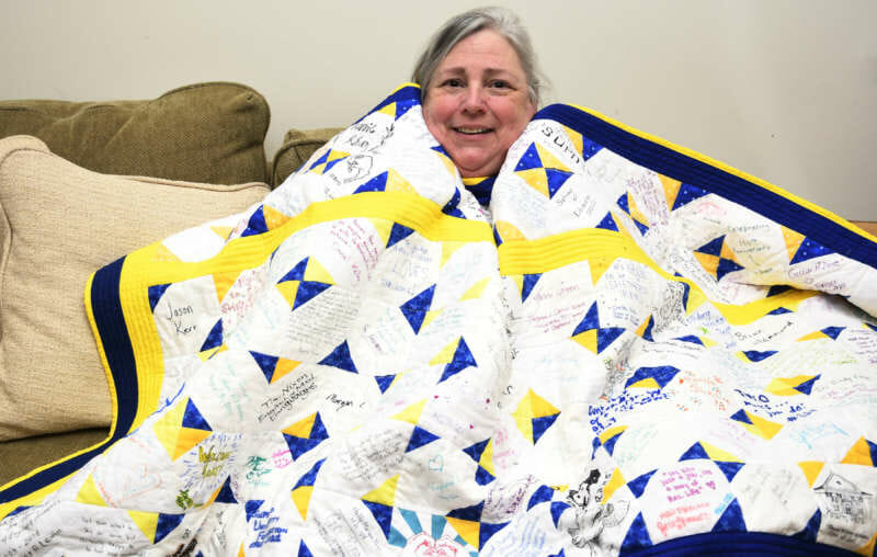 Photo of Rhonda Donaldson wrapped in the signature quilt she made.