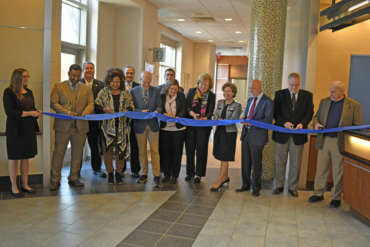 Photo of a group of people lined up cutting ribbon.