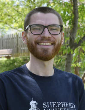 Photo of Andrew Price smiling, looking at the camera, with trees in the background.