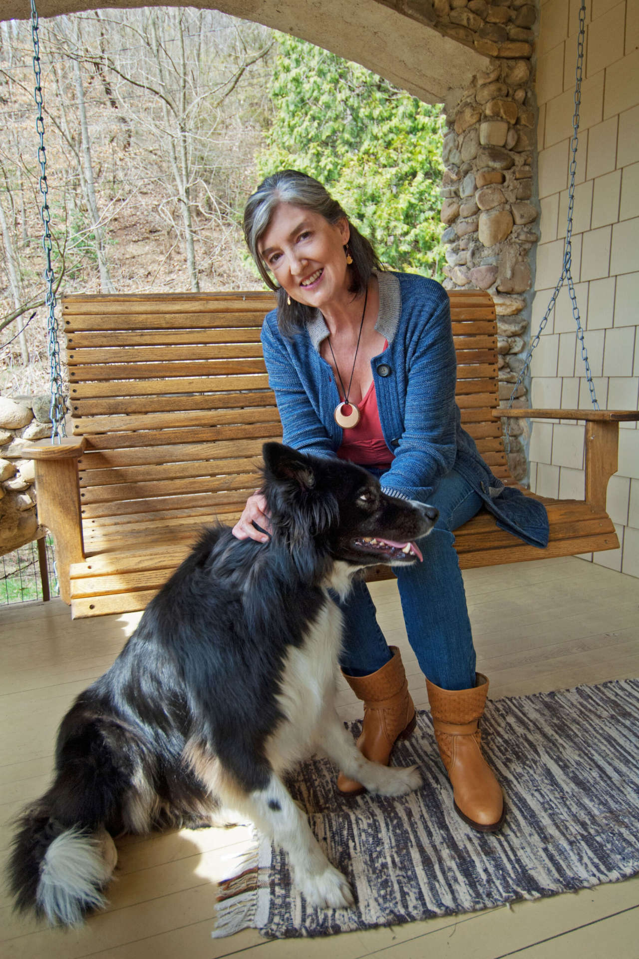 Barbara Kingsolver sitting on porch swing petting collie dog.
