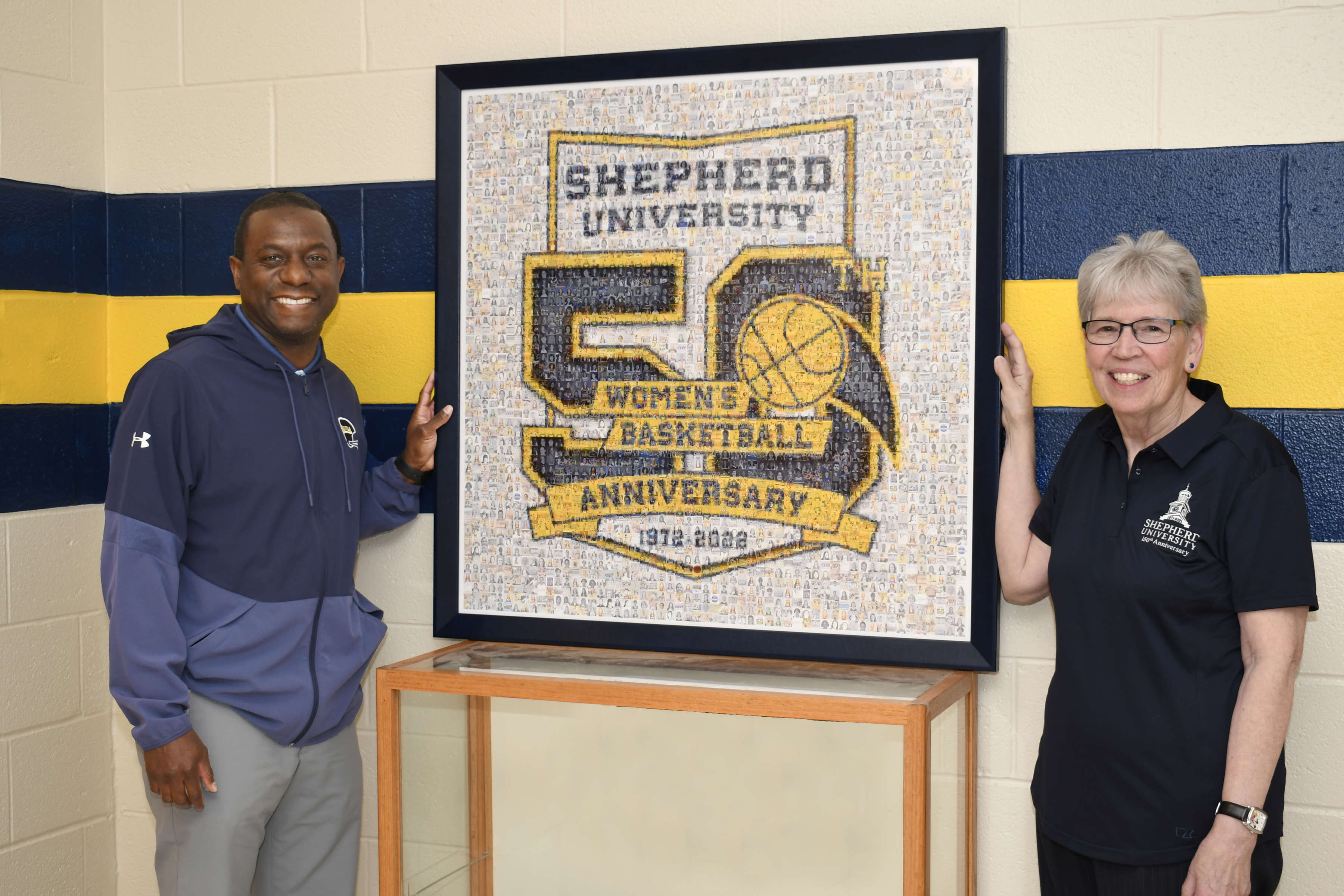 Photo of Chauncey Winbush and Lin Staub standing beside women's basketball 50th anniversary mosaic looking at camera smiling.