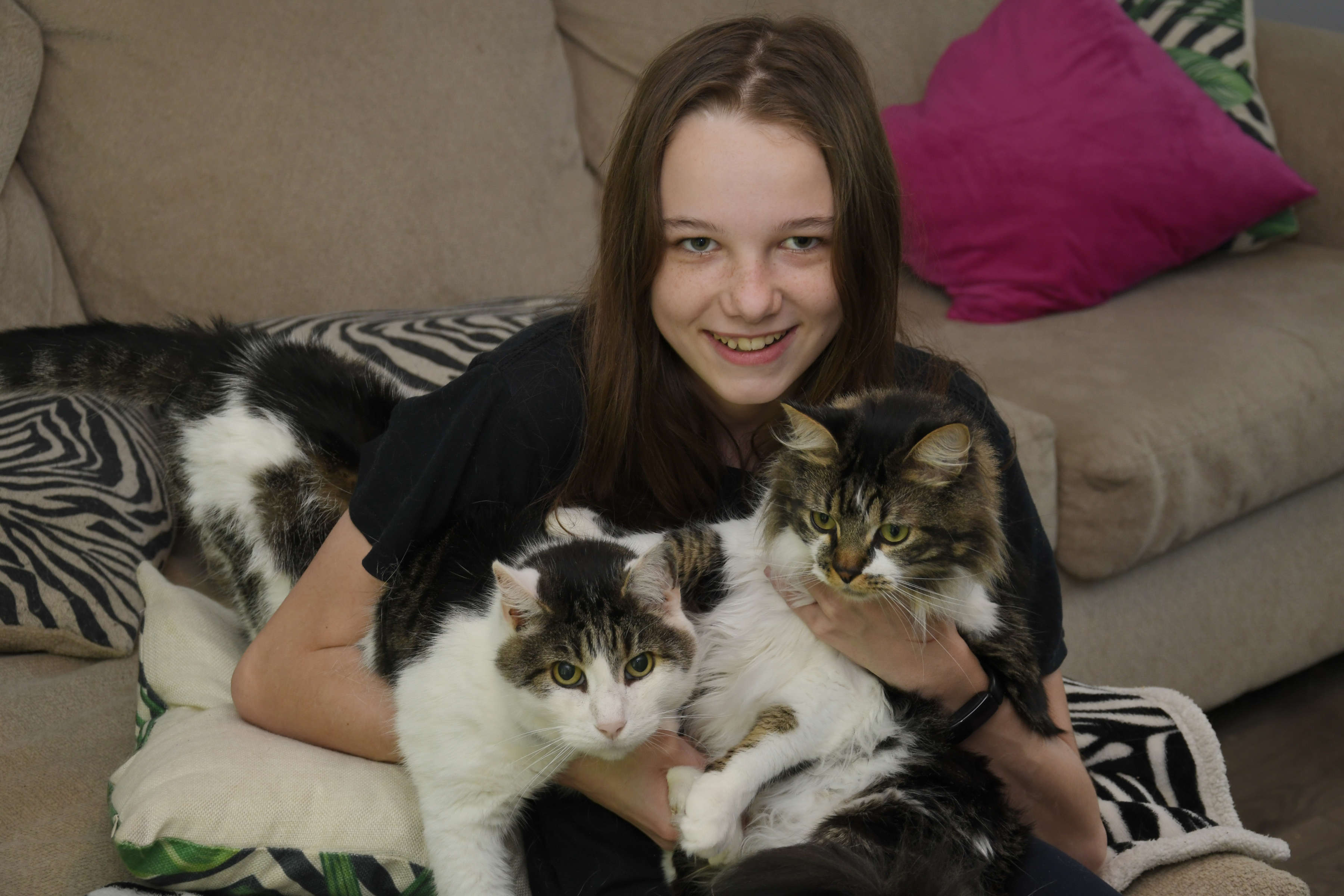 Photo of Piper Dotson holding her cats Oliver and Jasper, smiling, looking at the camera.