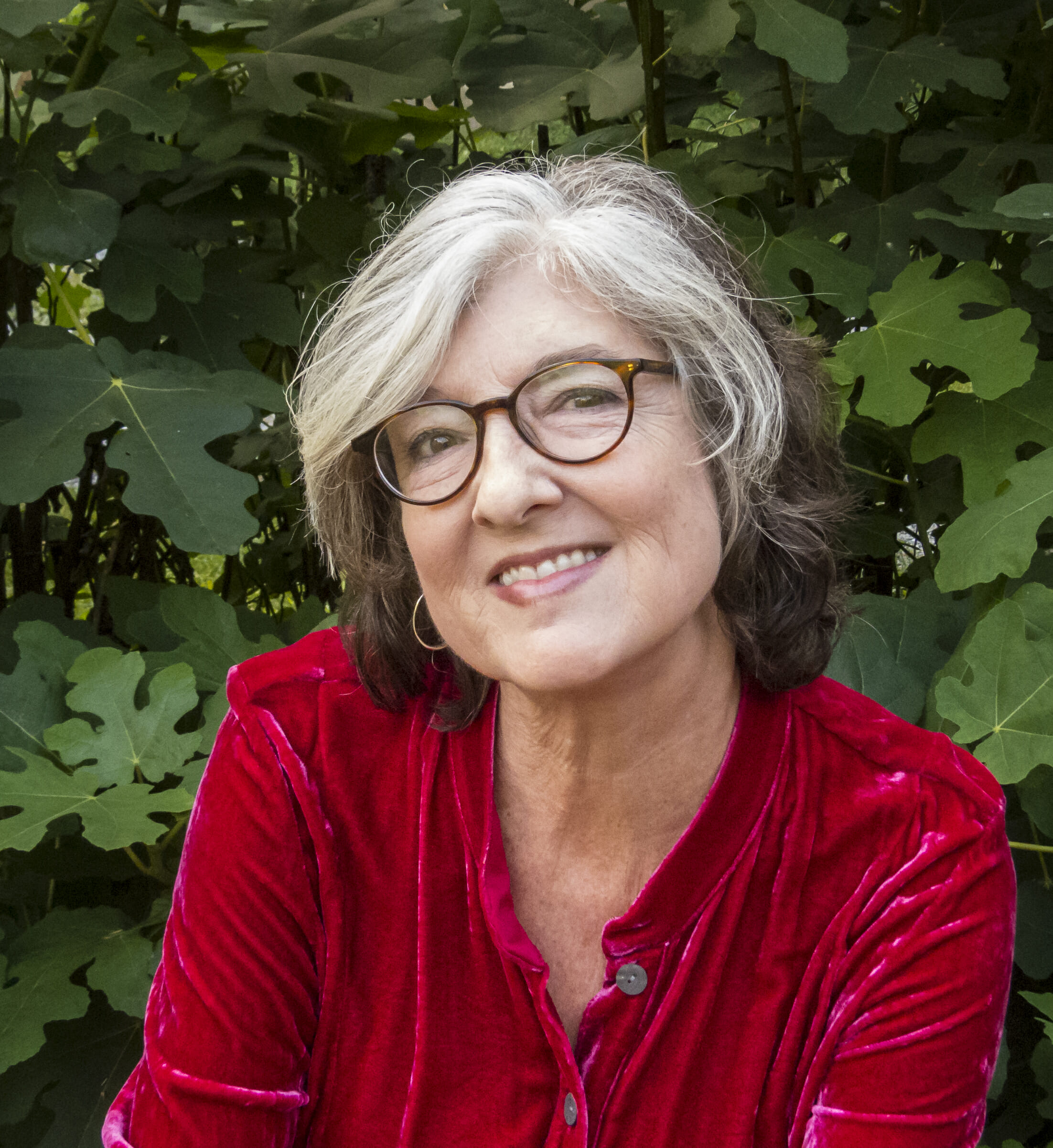Barbara Kingsolver smiling, looking at the camera, in front of foliage.