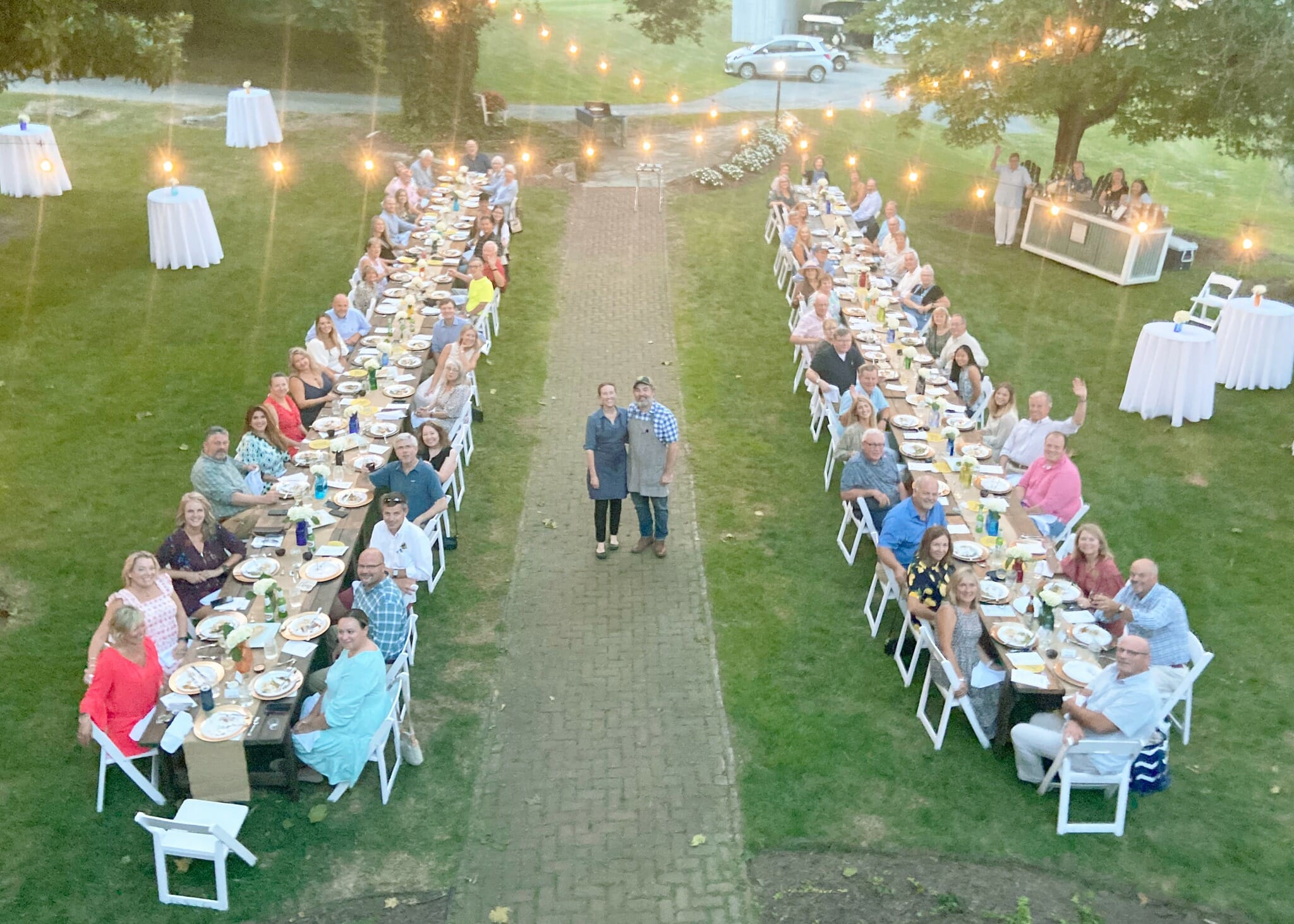 Photo of entire group at farm to table dinner sitting at two long tables with the chefs standing in the middle.