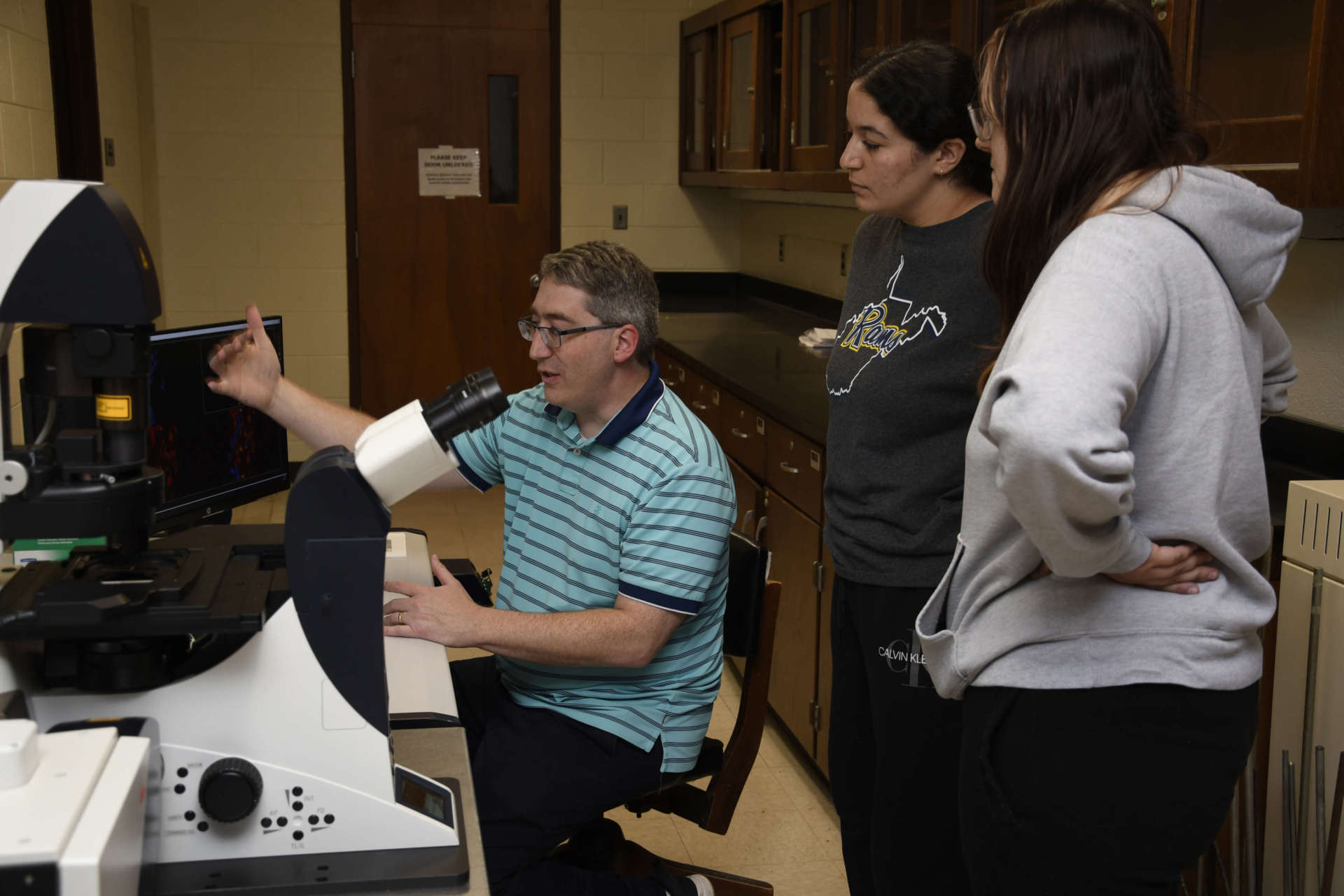 Photo of Conor Sipe showing Ronaida Ammari and Erika Voges the confocal microscope.