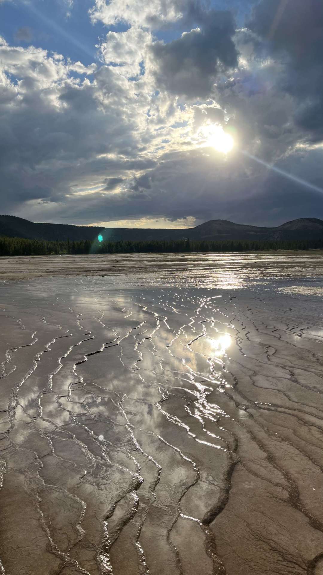 Photo of sun shining through clouds on water with mountains in the background at Yellowstone.