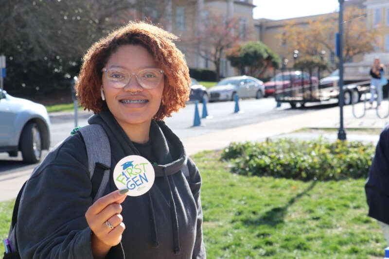 Young woman holding sticker that reads First Gen on a sunny day 
