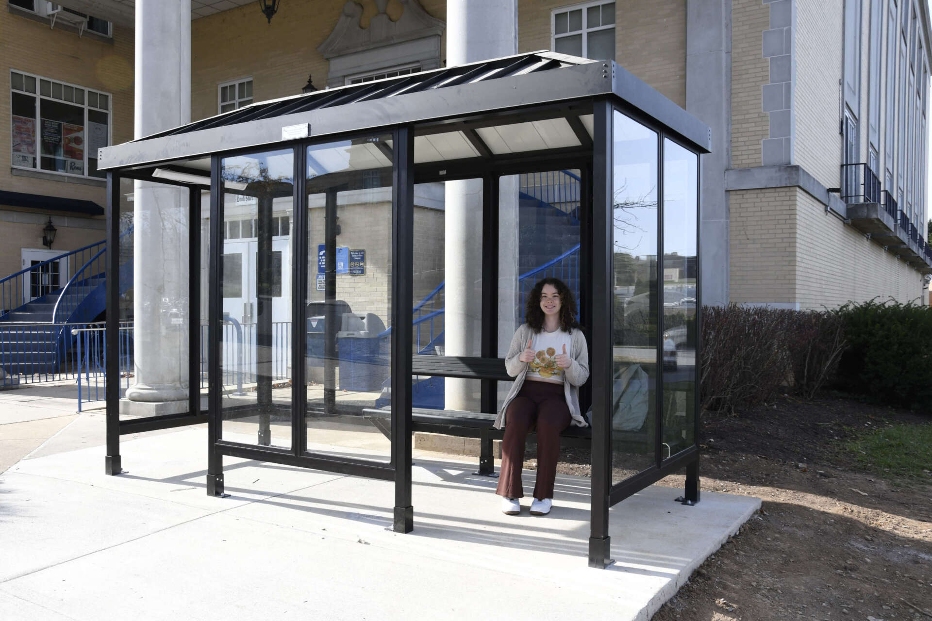 Student sitting in the new bus shelter giving a thumbs up.