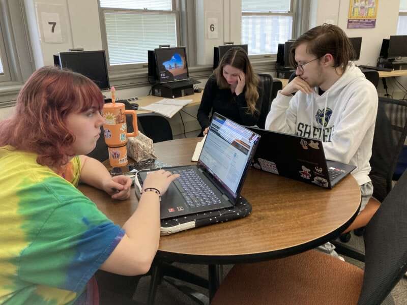 Photo of students in English true crime class working at a table on computers.