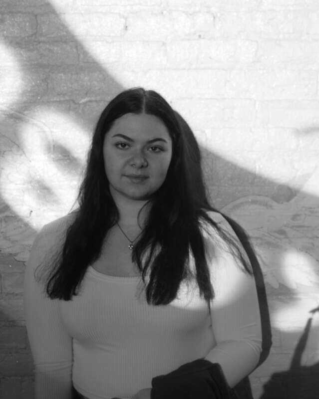 Black and white photo of a young woman standing against the wall